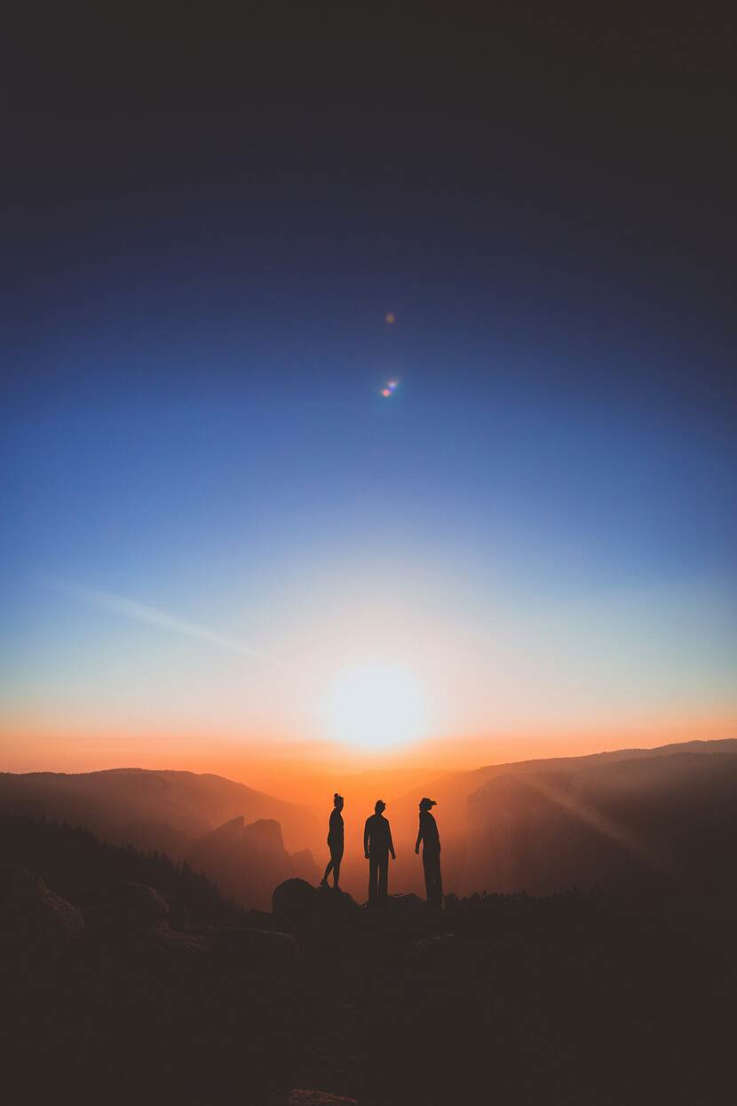 Drie mensen praten bij een zonsondergang